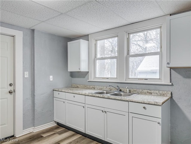 kitchen with a sink, light wood-type flooring, light countertops, white cabinetry, and a paneled ceiling