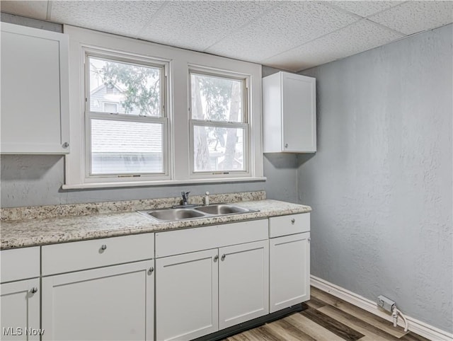 kitchen with wood finished floors, baseboards, a drop ceiling, a sink, and light countertops