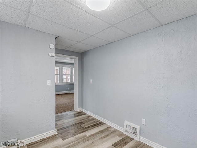 unfurnished room with a drop ceiling, visible vents, baseboards, and wood finished floors