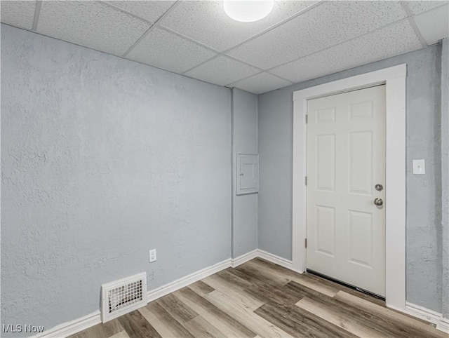 unfurnished room featuring wood finished floors, visible vents, baseboards, a drop ceiling, and a textured wall