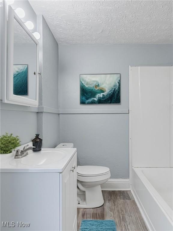 full bathroom featuring vanity, wood finished floors, baseboards, a textured ceiling, and toilet