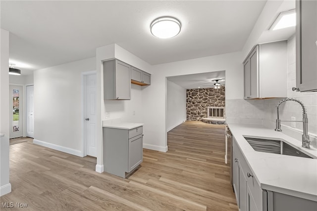 kitchen with gray cabinetry, sink, light hardwood / wood-style flooring, stainless steel dishwasher, and decorative backsplash