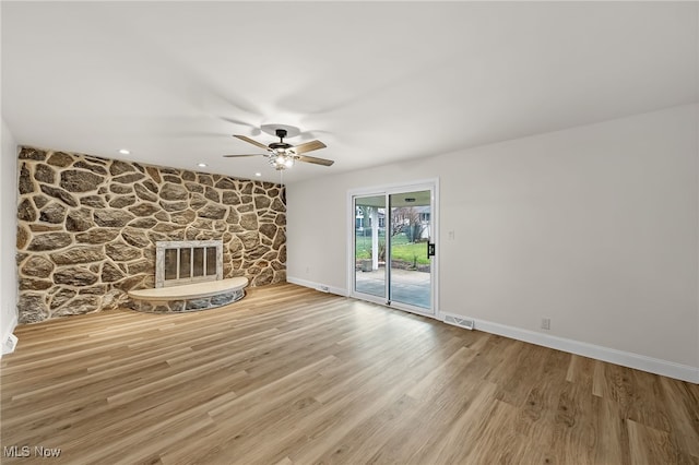 unfurnished living room featuring hardwood / wood-style flooring, a stone fireplace, and ceiling fan