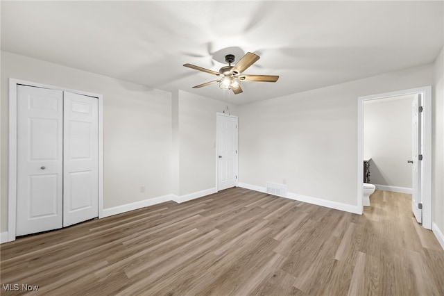 unfurnished bedroom featuring a closet, ensuite bathroom, light hardwood / wood-style flooring, and ceiling fan