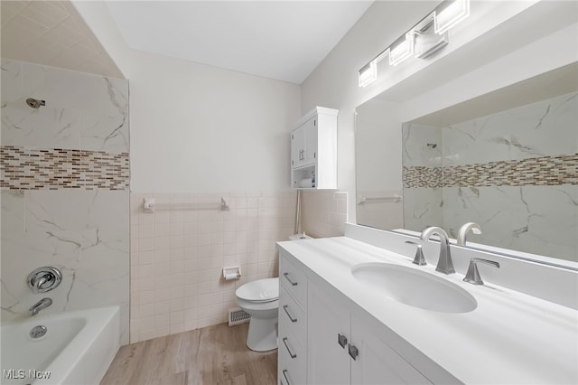 full bathroom with hardwood / wood-style floors, vanity, tiled shower / bath combo, toilet, and tile walls