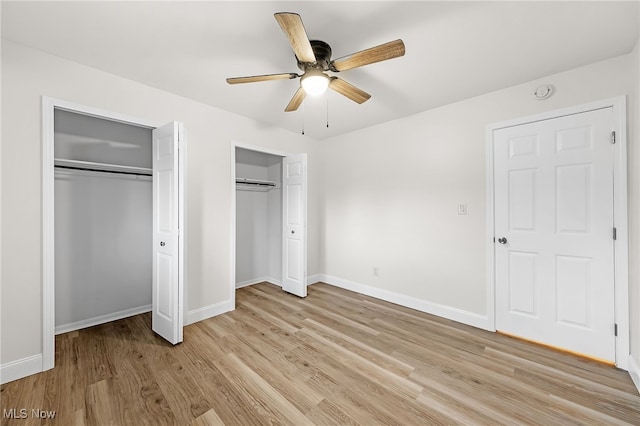 unfurnished bedroom featuring light hardwood / wood-style flooring, ceiling fan, and multiple closets