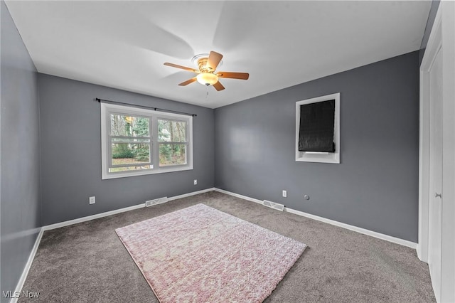 unfurnished room featuring a ceiling fan, dark colored carpet, visible vents, and baseboards