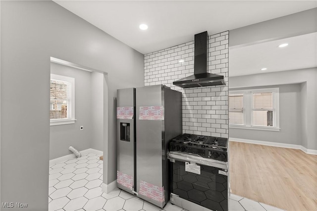 kitchen with wall chimney exhaust hood, light hardwood / wood-style flooring, stainless steel appliances, and tasteful backsplash