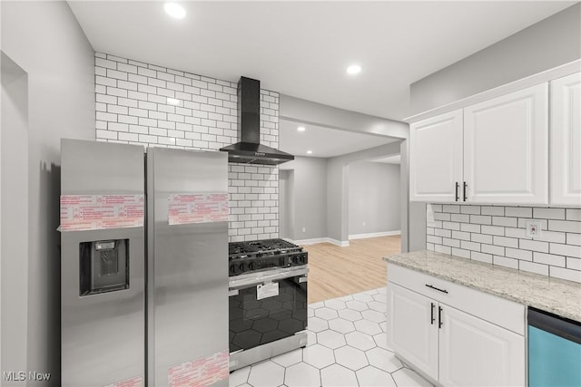 kitchen featuring light stone countertops, appliances with stainless steel finishes, wall chimney exhaust hood, white cabinets, and light hardwood / wood-style floors