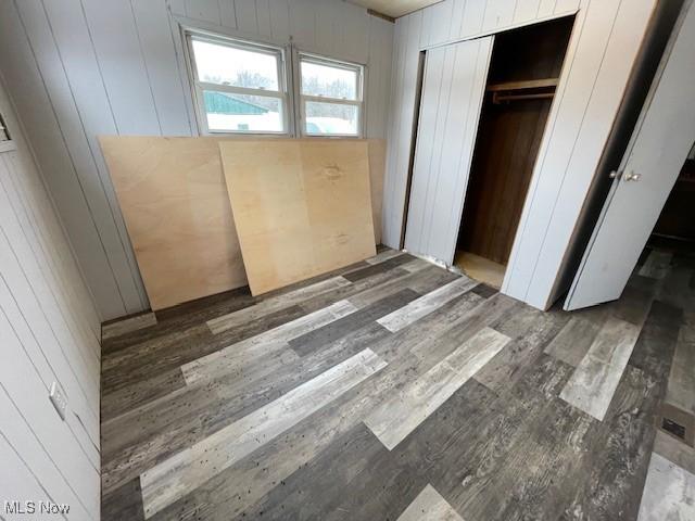 unfurnished bedroom with dark wood-type flooring, wooden walls, and a closet