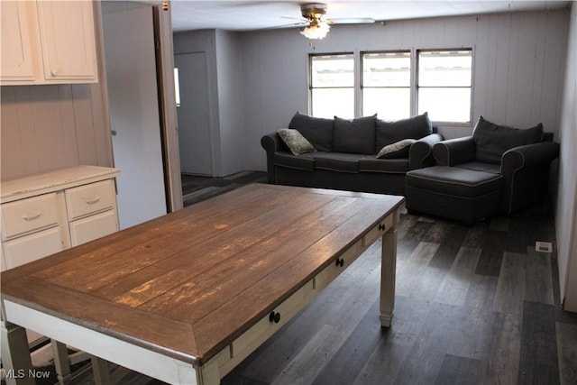 living room featuring wood walls, ceiling fan, and dark wood-type flooring