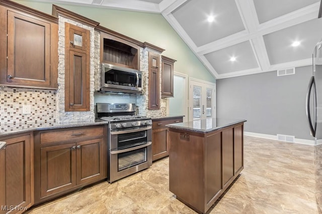 kitchen featuring a center island, stainless steel appliances, tasteful backsplash, lofted ceiling with beams, and dark stone counters