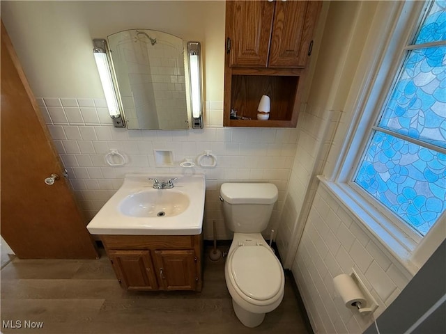 bathroom featuring wood-type flooring, toilet, vanity, and tile walls