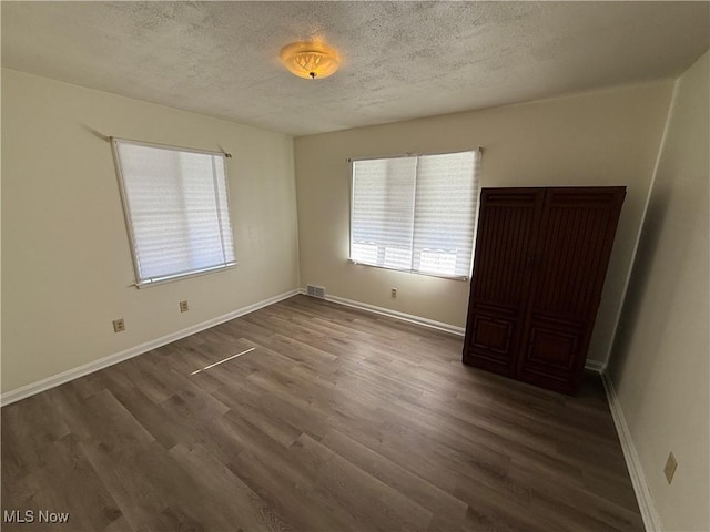 unfurnished room featuring a textured ceiling and dark hardwood / wood-style flooring