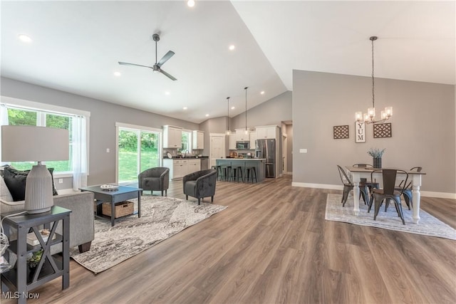 living room featuring high vaulted ceiling, ceiling fan with notable chandelier, and hardwood / wood-style flooring