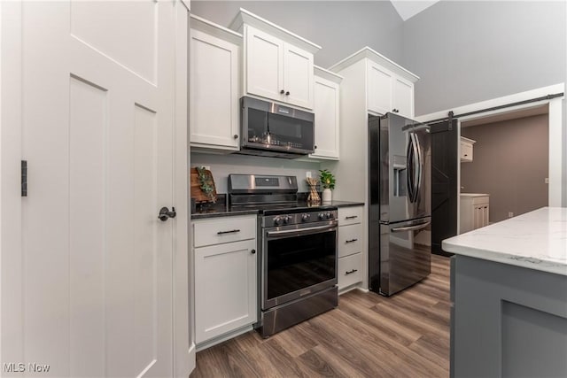 kitchen featuring white cabinets, a barn door, dark stone countertops, dark hardwood / wood-style flooring, and stainless steel appliances