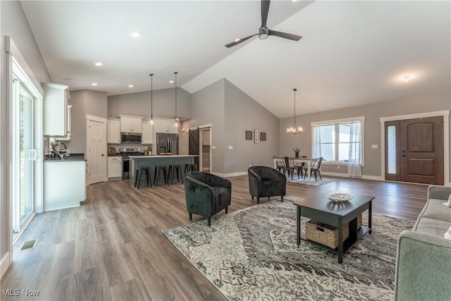 living room featuring light hardwood / wood-style flooring, high vaulted ceiling, and ceiling fan with notable chandelier