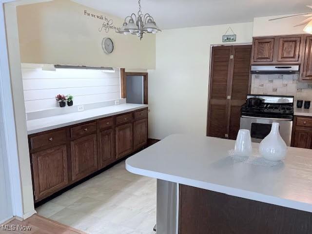 kitchen featuring ceiling fan with notable chandelier, dark brown cabinets, tasteful backsplash, gas range, and decorative light fixtures