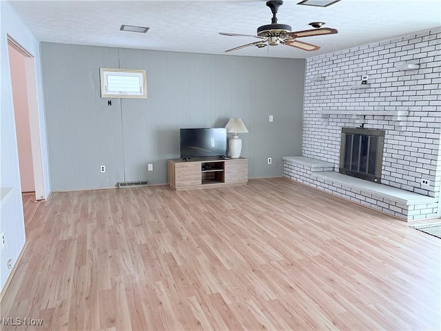 unfurnished living room with light hardwood / wood-style flooring, ceiling fan, a textured ceiling, a brick fireplace, and wood walls