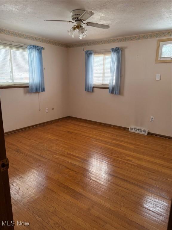 empty room featuring plenty of natural light, hardwood / wood-style floors, a textured ceiling, and ceiling fan