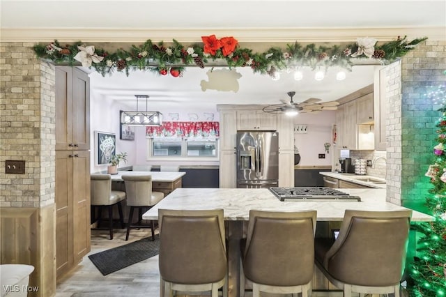 kitchen with kitchen peninsula, stainless steel appliances, sink, light hardwood / wood-style floors, and hanging light fixtures