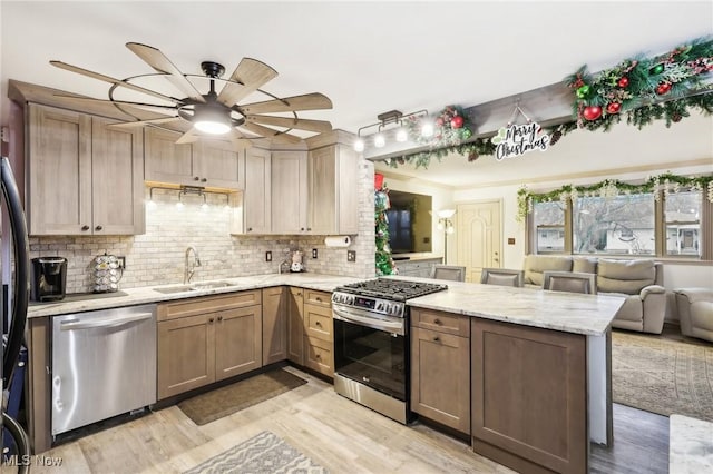 kitchen featuring sink, stainless steel appliances, tasteful backsplash, kitchen peninsula, and light wood-type flooring