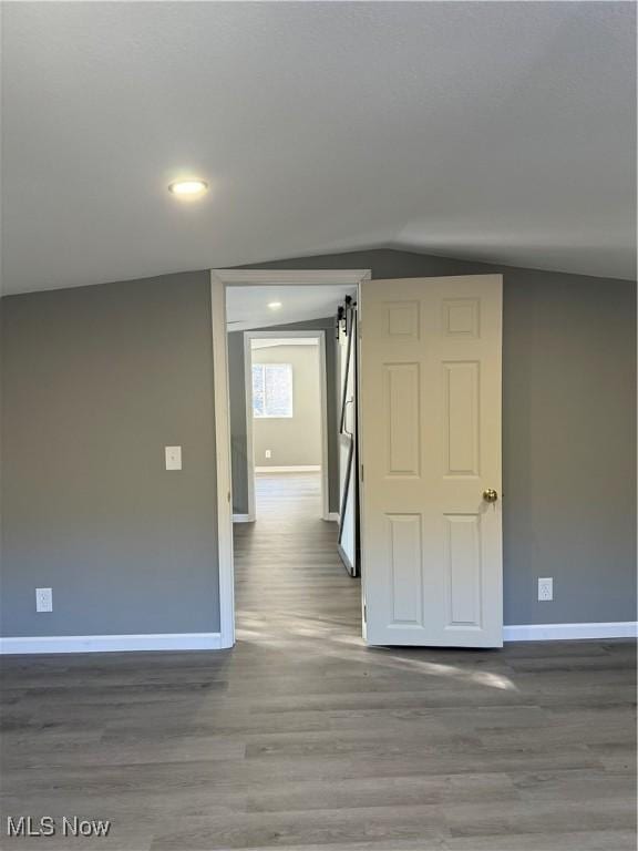 spare room with a barn door, wood-type flooring, and lofted ceiling