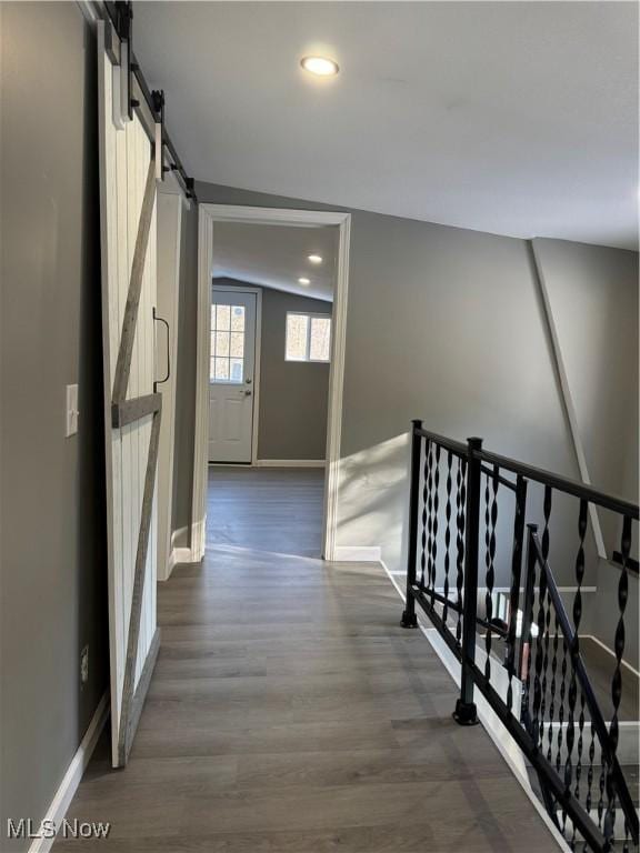 hallway with a barn door, dark hardwood / wood-style flooring, and vaulted ceiling