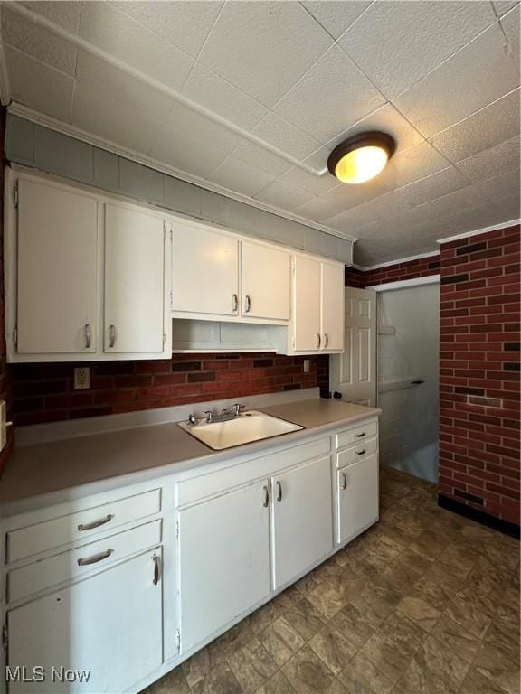 kitchen featuring sink, white cabinets, and brick wall