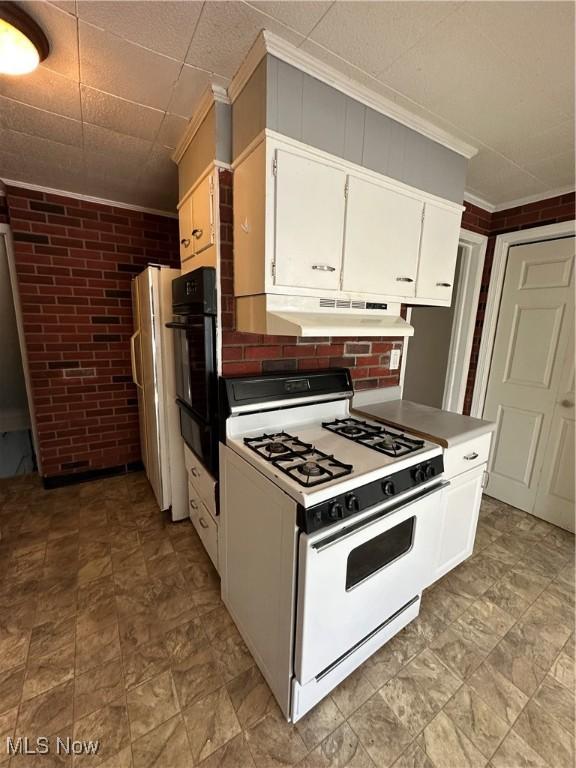 kitchen featuring white range oven, crown molding, white cabinets, and brick wall