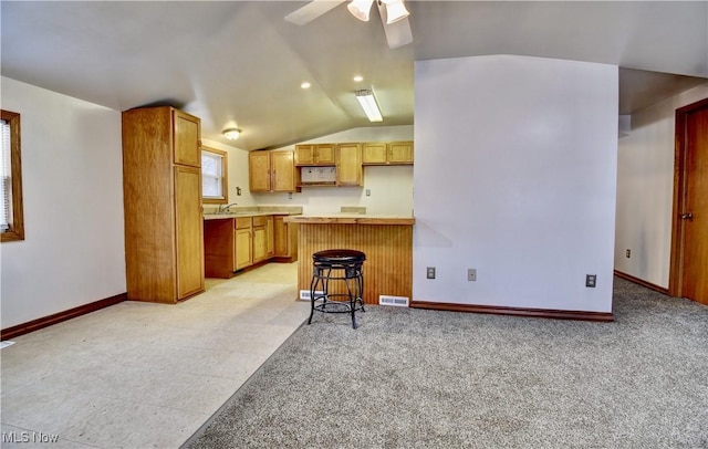 kitchen with kitchen peninsula, a breakfast bar, vaulted ceiling, ceiling fan, and sink