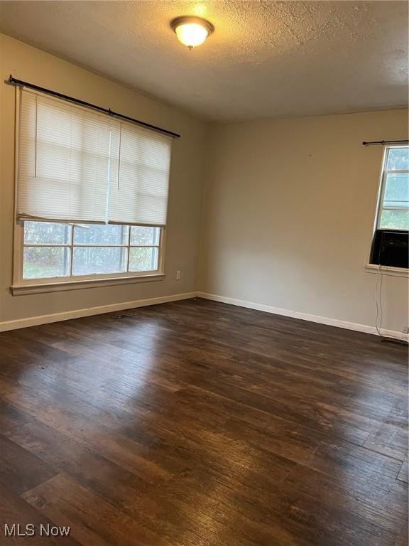 empty room with a textured ceiling, plenty of natural light, and dark wood-type flooring