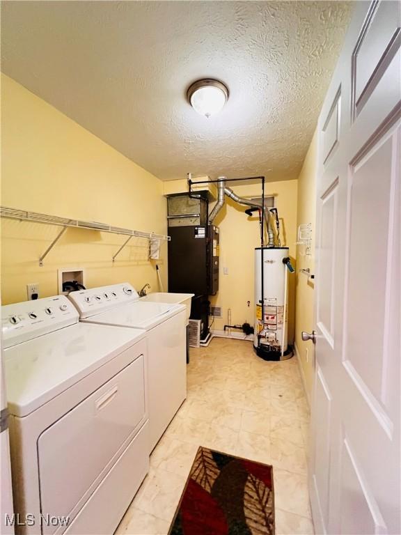 clothes washing area with a textured ceiling, heating unit, washer and clothes dryer, and water heater