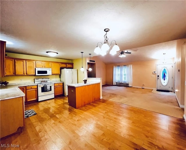 kitchen with light wood-type flooring, white appliances, ceiling fan with notable chandelier, decorative light fixtures, and a kitchen island