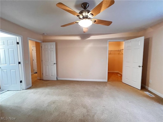 unfurnished bedroom featuring a closet, a walk in closet, light colored carpet, and ceiling fan