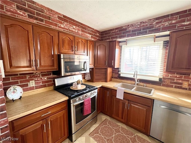 kitchen with a textured ceiling, brick wall, sink, and appliances with stainless steel finishes