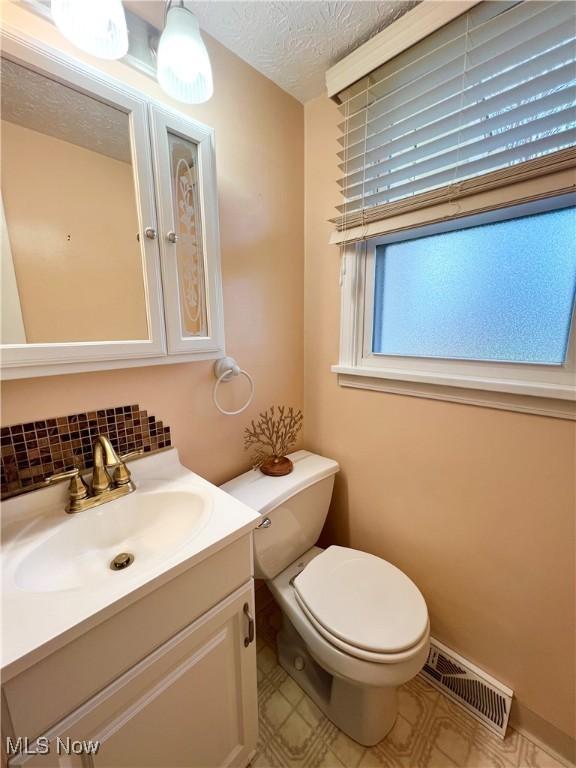 bathroom featuring vanity, toilet, decorative backsplash, and a textured ceiling