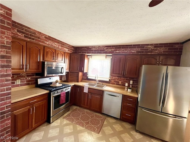 kitchen with sink, stainless steel appliances, a textured ceiling, and brick wall