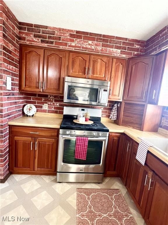 kitchen with appliances with stainless steel finishes and brick wall