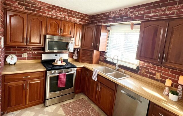 kitchen featuring brick wall, appliances with stainless steel finishes, butcher block countertops, and sink