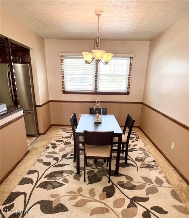 carpeted dining space featuring plenty of natural light, a textured ceiling, and a chandelier