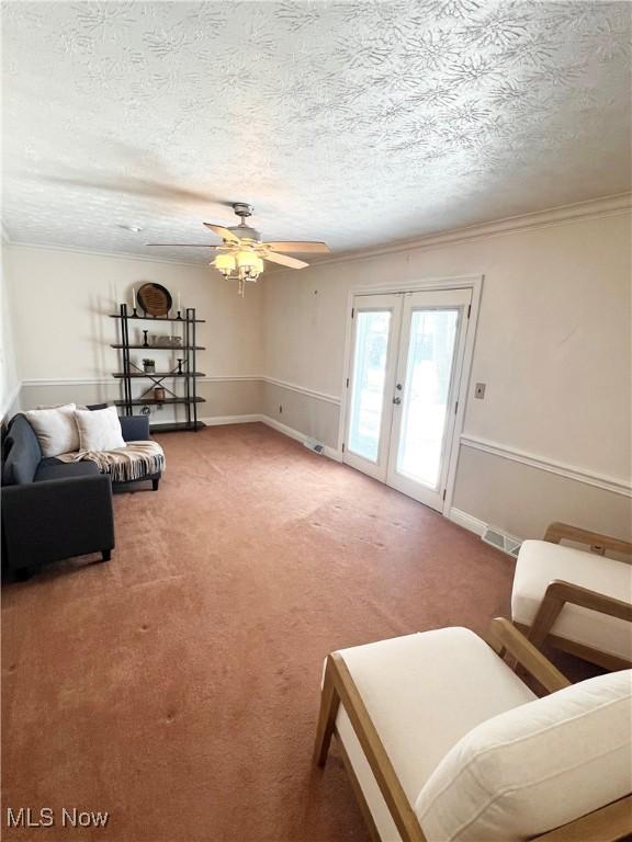 carpeted living room with ceiling fan, french doors, crown molding, and a textured ceiling