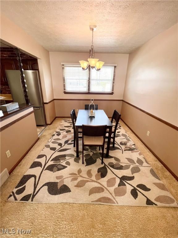 carpeted dining area featuring a textured ceiling and an inviting chandelier