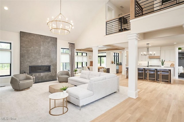 living room with decorative columns, plenty of natural light, a towering ceiling, and light wood-type flooring