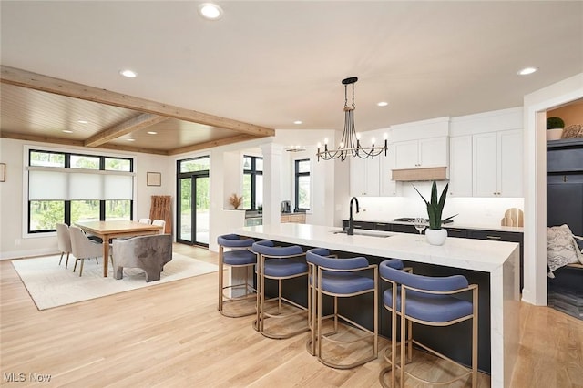 kitchen with a kitchen island with sink, sink, decorative light fixtures, light hardwood / wood-style flooring, and white cabinetry