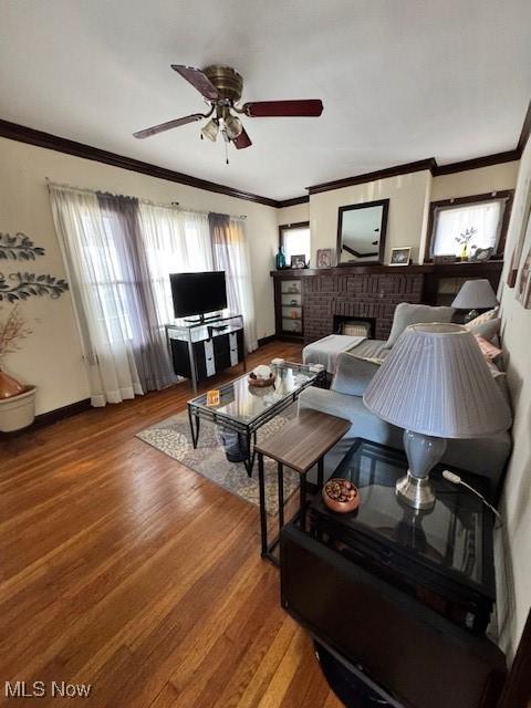 living room featuring crown molding, ceiling fan, a fireplace, and wood-type flooring