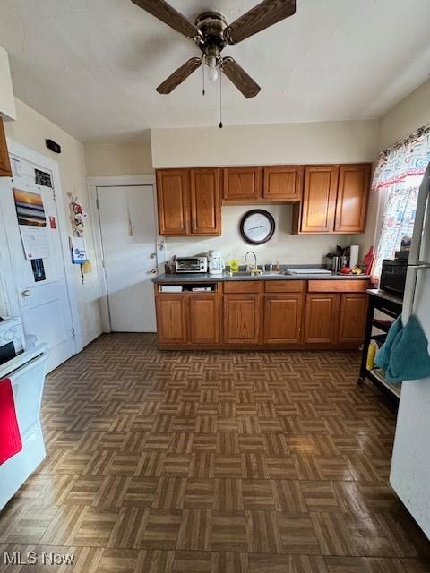 kitchen with dark parquet flooring, stove, ceiling fan, and sink