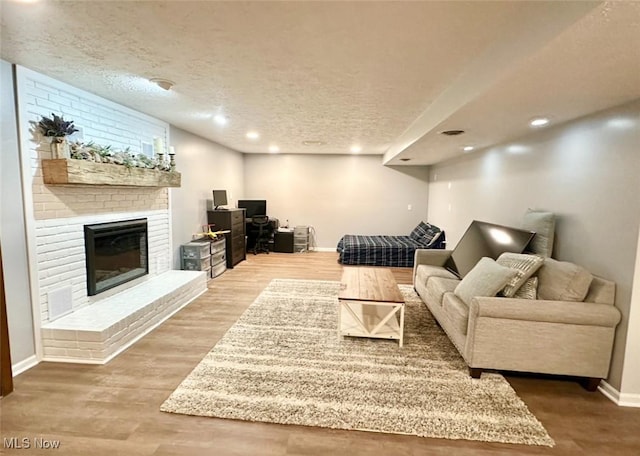 living room with wood-type flooring, a textured ceiling, and a brick fireplace