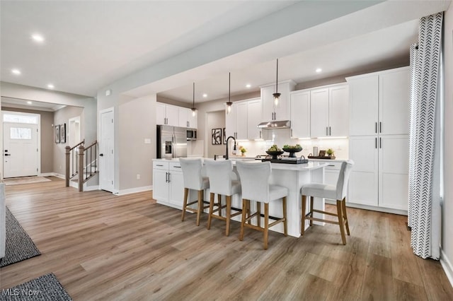 kitchen featuring a center island with sink, white cabinetry, hanging light fixtures, and stainless steel appliances