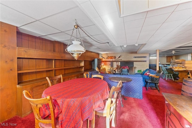 dining area featuring carpet flooring, ceiling fan, and wood walls